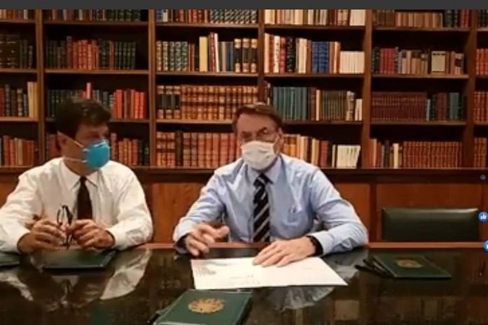 Com máscaras no rosto, Bolsonaro faz transmissão ao vivo com ministro da Saúde.