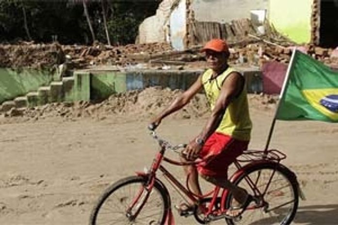 Em Alagoas, torcedor passa de bicicleta em frente à rua destruída completamente destruída