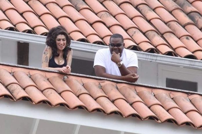Amy chega a hotel no Rio com seguranças e sorri da sacada