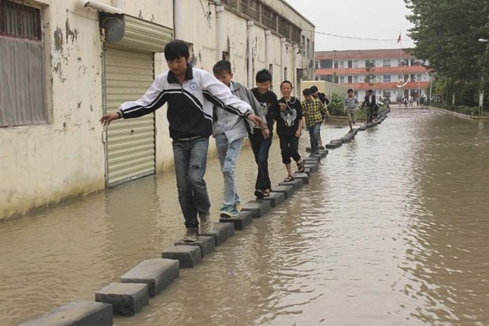 Alunos improvisam para cruzar rua que há anos está alagada na China