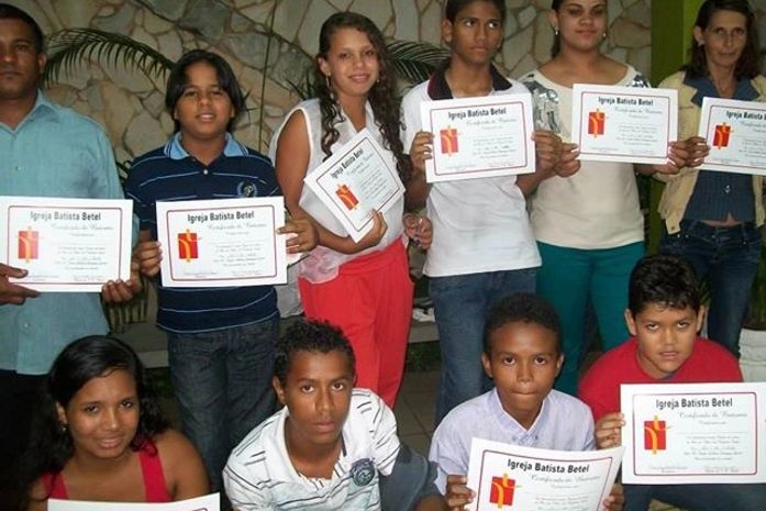 Adolescentes, jovens e adultos exibem certificados após o batismo