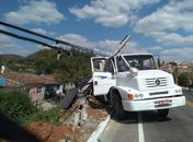 Motorista perde controle de caminhão, colide em poste e fica pendurado em ribanceira 