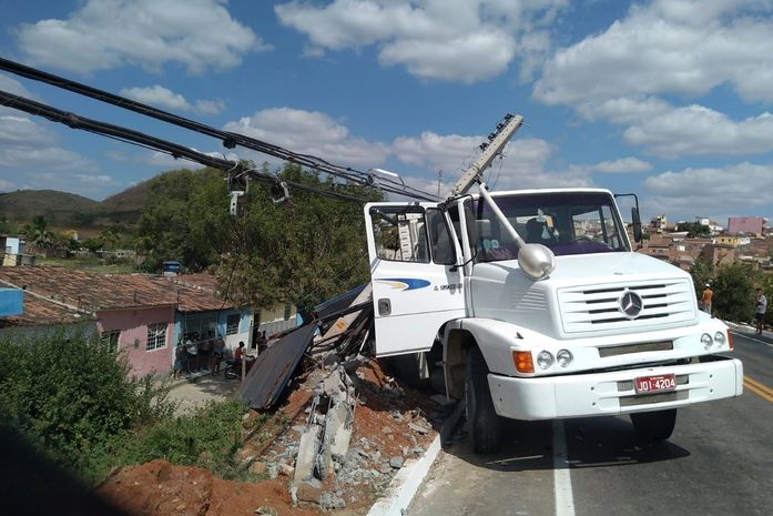 Motorista perde controle de caminhão, colide em poste e fica pendurado em ribanceira