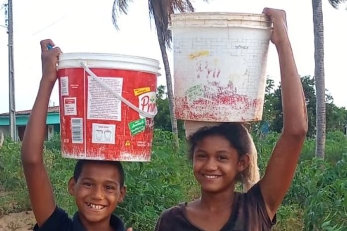 Lata d’água na cabeça,  lá vai o Carlos, 10 anos, e a irmã, sob o sol quente do Quilombo. Não tem água encanada nas torneiras.