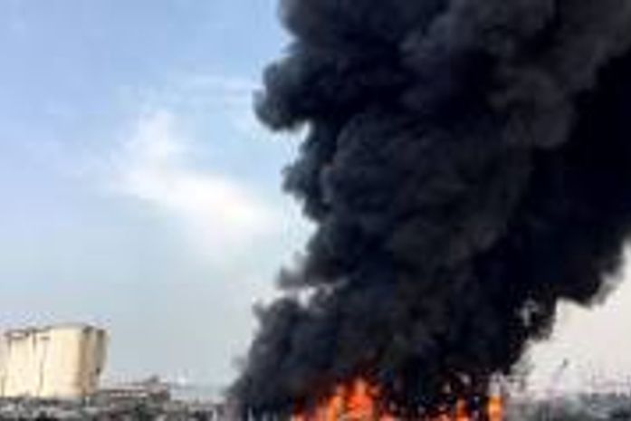Chamas atingem um armazém onde estão estocados óleo para motor e rodas de carro; densas colunas de fumaça negra podem ser vistas.
