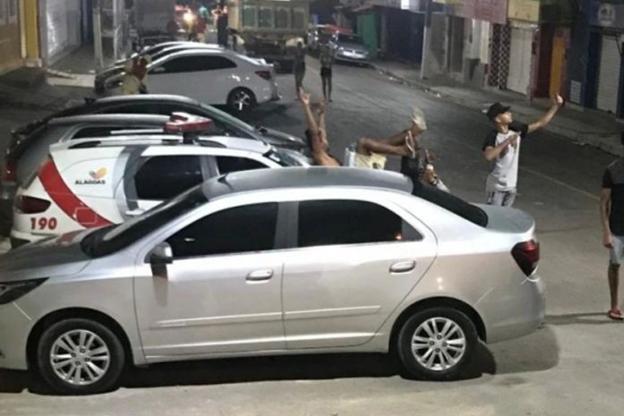 Com bebidas nas mãos, jovens subiram em viatura para tirar fotos.