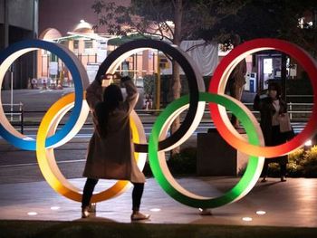 Mulheres com máscara de proteção tiram foto com símbolo olímpico em Tóquio